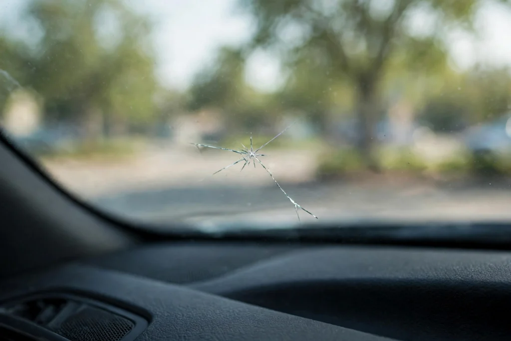 Close-up of a cracked windshield with a star-shaped chip viewed from inside a parked car, soft daylight, sharp focus on the damage